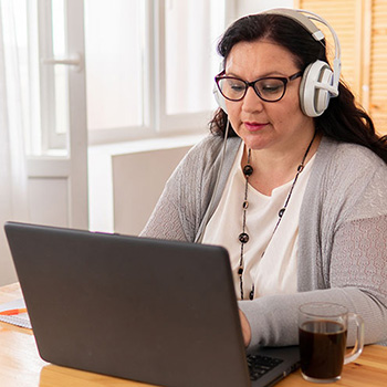 Mature woman wearing glasses and a headset, using a laptop to work at home.